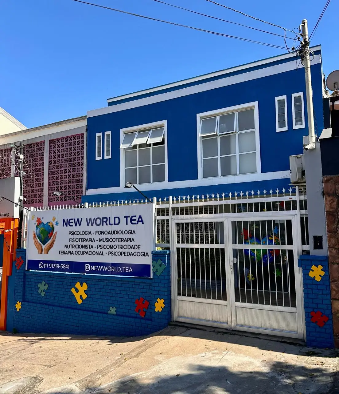 Fachada azul da clínica New World TEA na Rua Colônia da Glória, com a placa das especialidades