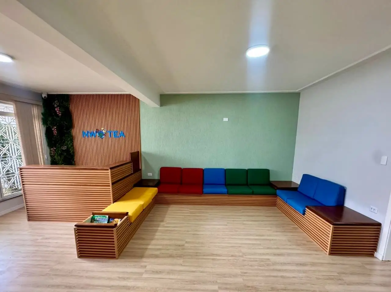 Recepção da clínica com sofás coloridos e painel de madeira com o logo da New World TEA